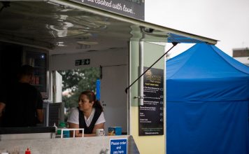 A food truck with staff serving at an outdoor festival with colorful tents.