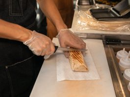 A close-up of a person's hands slicing a shawarma on a kitchen counter, showcasing food preparation.