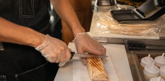 A close-up of a person's hands slicing a shawarma on a kitchen counter, showcasing food preparation.