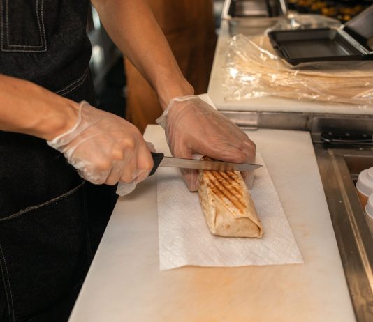 A close-up of a person's hands slicing a shawarma on a kitchen counter, showcasing food preparation.