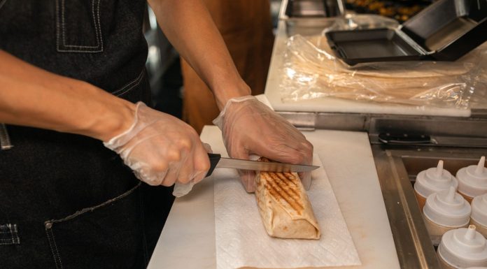 A close-up of a person's hands slicing a shawarma on a kitchen counter, showcasing food preparation.