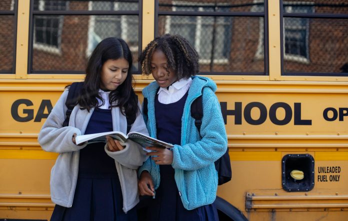 best-high-schools-bayonne-ranked-2026 Multiethnic schoolchildren in uniforms watching exercise book near yellow school bus reflecting building in town