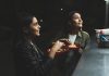 Two women joyfully ordering tacos at a vibrant nighttime street stand.