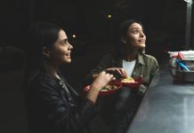 Two women joyfully ordering tacos at a vibrant nighttime street stand.