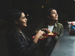 Two women joyfully ordering tacos at a vibrant nighttime street stand.