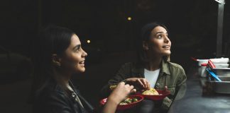 Two women joyfully ordering tacos at a vibrant nighttime street stand.