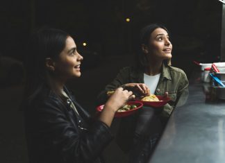 Two women joyfully ordering tacos at a vibrant nighttime street stand.