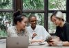 BREAKING: 10 Ways to Make Friends as an Adult in Jersey City Group of cheerful friends laughing at funny meme while surfing social media on smartphone sitting at table with laptop in modern cafe