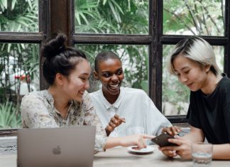 BREAKING: 10 Ways to Make Friends as an Adult in Jersey City Group of cheerful friends laughing at funny meme while surfing social media on smartphone sitting at table with laptop in modern cafe