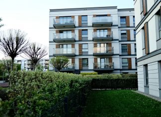 Contemporary apartment complex with balconies and lush garden in urban setting.