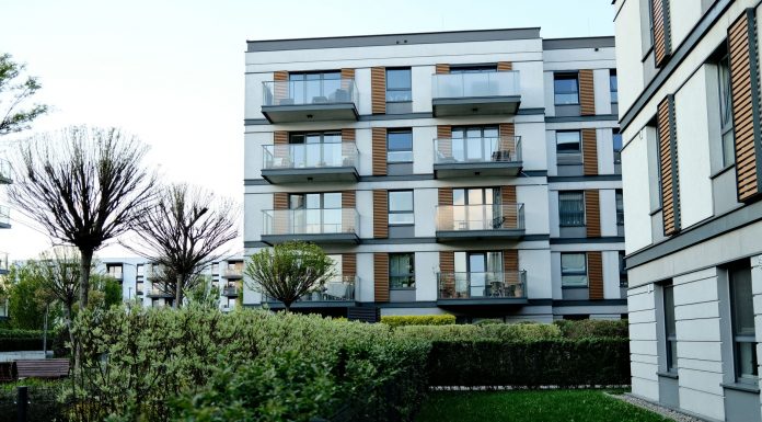 Contemporary apartment complex with balconies and lush garden in urban setting.