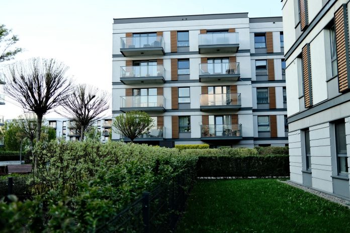 Contemporary apartment complex with balconies and lush garden in urban setting.