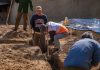 Volunteers working together to dig a trench at a construction site in daylight.