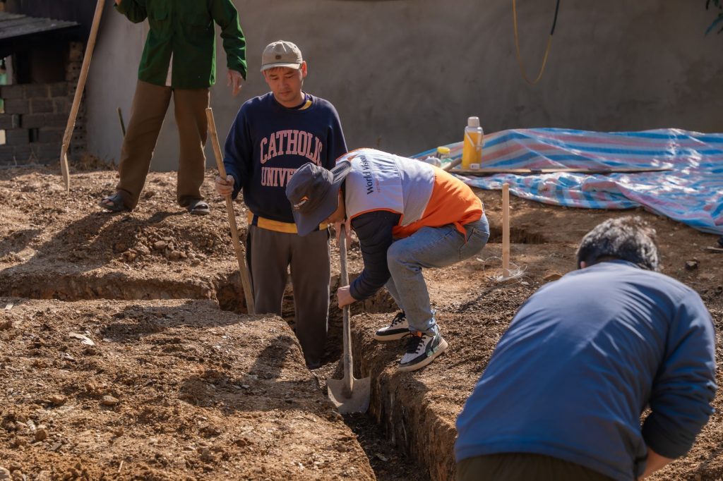Volunteers working together to dig a trench at a construction site in daylight.