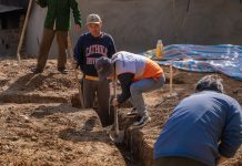 Volunteers working together to dig a trench at a construction site in daylight.