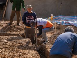Volunteers working together to dig a trench at a construction site in daylight.