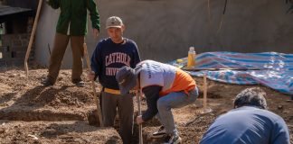 Volunteers working together to dig a trench at a construction site in daylight.