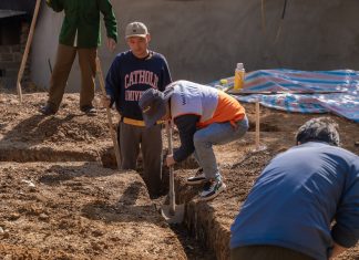 Volunteers working together to dig a trench at a construction site in daylight.