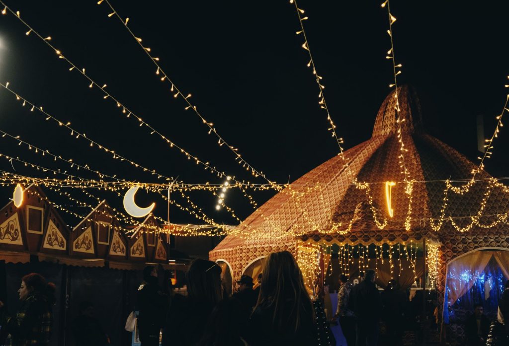 A vibrant evening market scene under string lights with people gathering in a lively atmosphere.