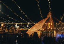 A vibrant evening market scene under string lights with people gathering in a lively atmosphere.