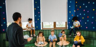 Preschool teacher leading storytime with children reading books in a colorful classroom setting.