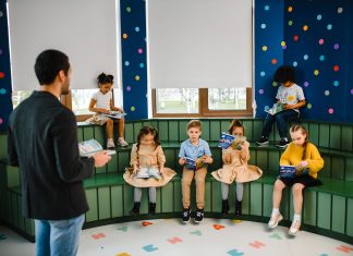 Preschool teacher leading storytime with children reading books in a colorful classroom setting.