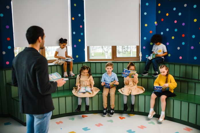 breaking-former-teacher-reads-newark-kids-to-brigh Preschool teacher leading storytime with children reading books in a colorful classroom setting.