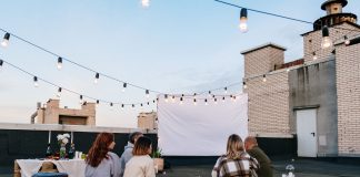 Friends enjoying a cozy evening movie on a rooftop with string lights and blankets.