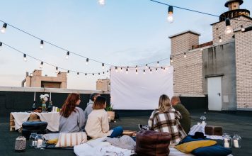 Friends enjoying a cozy evening movie on a rooftop with string lights and blankets.