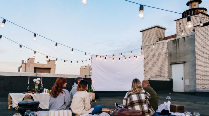 Friends enjoying a cozy evening movie on a rooftop with string lights and blankets.