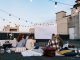 Friends enjoying a cozy evening movie on a rooftop with string lights and blankets.