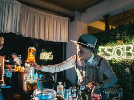 Bartender skillfully mixing a cocktail in a trendy neon-lit bar setting with lively ambiance.