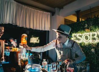 Bartender skillfully mixing a cocktail in a trendy neon-lit bar setting with lively ambiance.