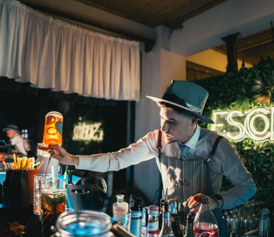 Bartender skillfully mixing a cocktail in a trendy neon-lit bar setting with lively ambiance.