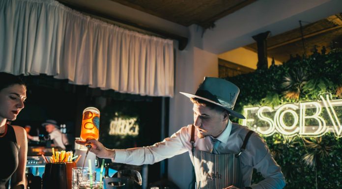 Bartender skillfully mixing a cocktail in a trendy neon-lit bar setting with lively ambiance.