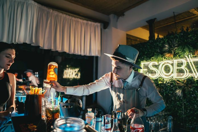 Bartender skillfully mixing a cocktail in a trendy neon-lit bar setting with lively ambiance.