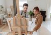 Man and woman collaborating on a painting in a bright art studio with an easel.