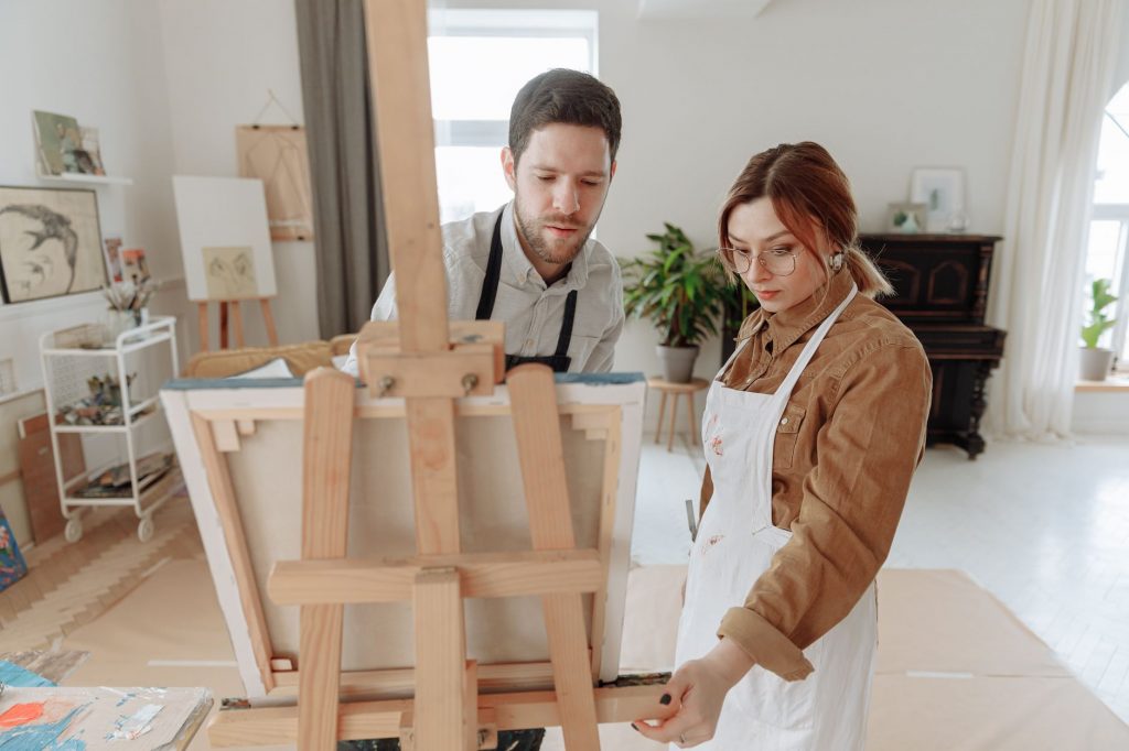 Man and woman collaborating on a painting in a bright art studio with an easel.