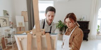 Man and woman collaborating on a painting in a bright art studio with an easel.