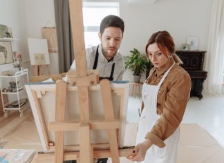Man and woman collaborating on a painting in a bright art studio with an easel.