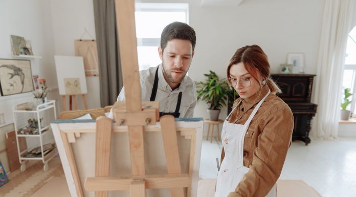Man and woman collaborating on a painting in a bright art studio with an easel.