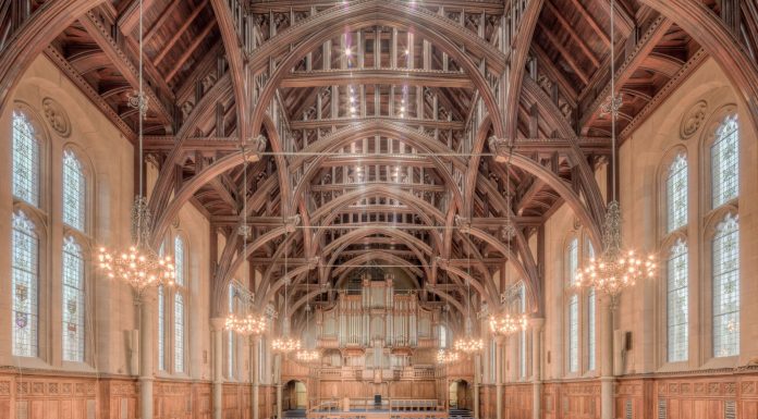 Elegant interior of a historic hall at the University of Manchester, showcasing intricate wooden beams and lighting.