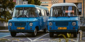 Two retro blue vans parked side by side in a city environment, showcasing classic design.