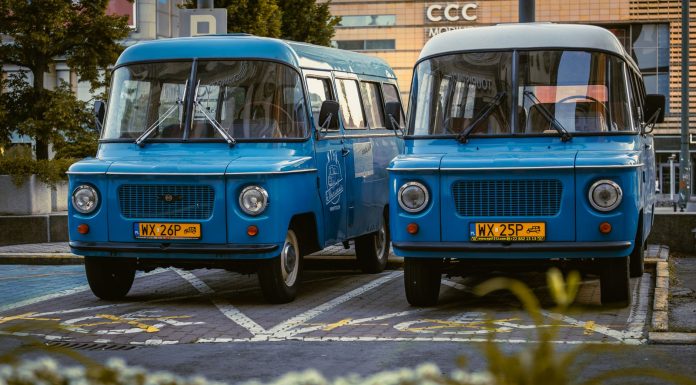 Two retro blue vans parked side by side in a city environment, showcasing classic design.