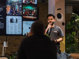A speaker holding a microphone addresses an audience indoors at a presentation event.