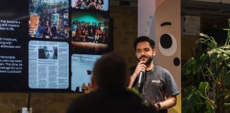 A speaker holding a microphone addresses an audience indoors at a presentation event.
