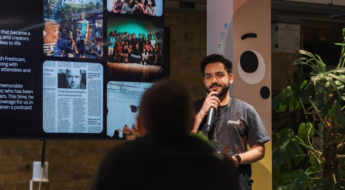 BREAKING: Jersey City Poetry Festival Moves to Mana, Features Obama Poet A speaker holding a microphone addresses an audience indoors at a presentation event.