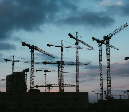 Multiple construction cranes silhouetted against the evening sky, capturing industrial progress.
