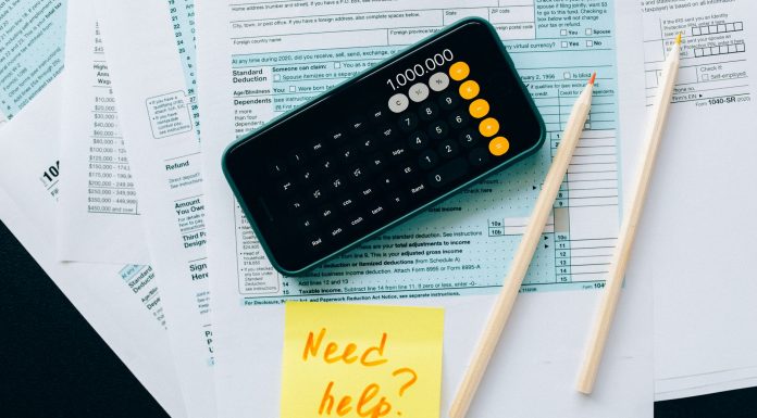Top view of financial papers with a calculator, pencils, and a note saying 'Need help?' indicating tax or accounting assistance.