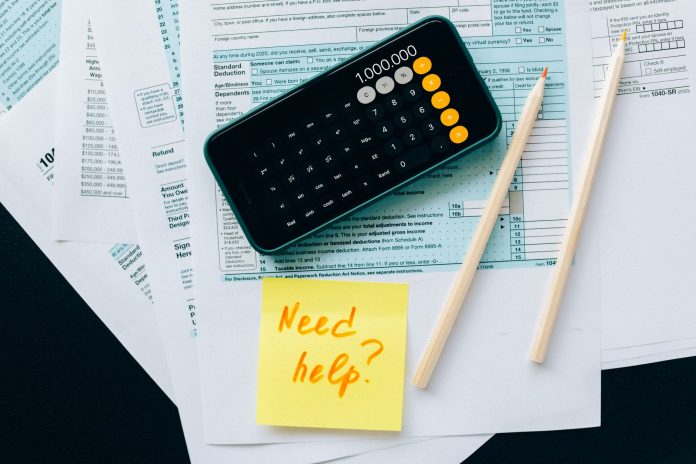 breaking-new-tool-helps-nj-families-claim-1-000-ch Top view of financial papers with a calculator, pencils, and a note saying 'Need help?' indicating tax or accounting assistance.